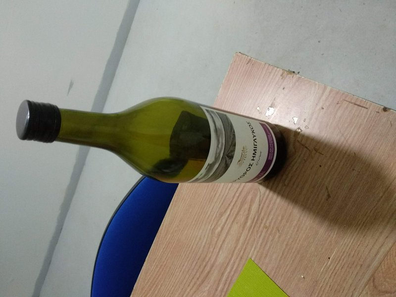 Olive green glass Greek wine bottle resting horizontally on a light wooden indoor table.