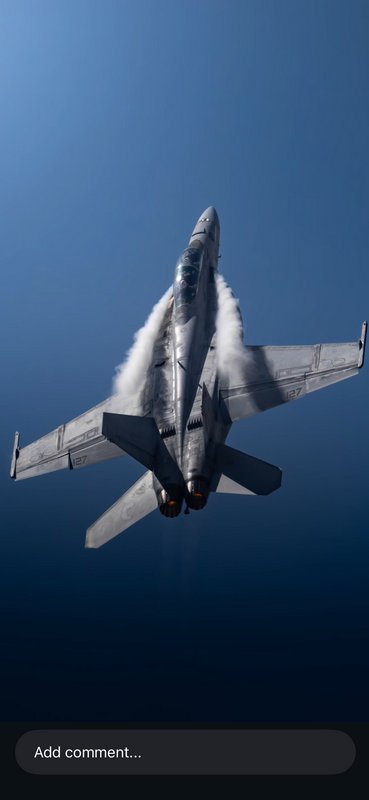 Military fighter jet ascending through a clear blue sky with white vapor trails.