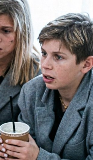 Close-up of teen boy with highlighted hair holding an iced drink, blonde woman seated beside him ...