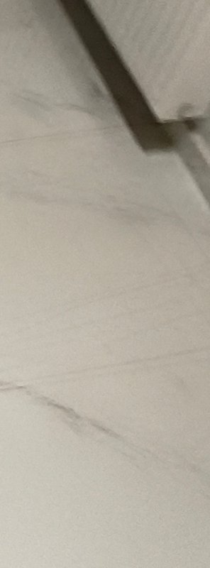 Blurry tilted view of light beige tiled indoor floor with a dark diagonal furniture leg shadow in...