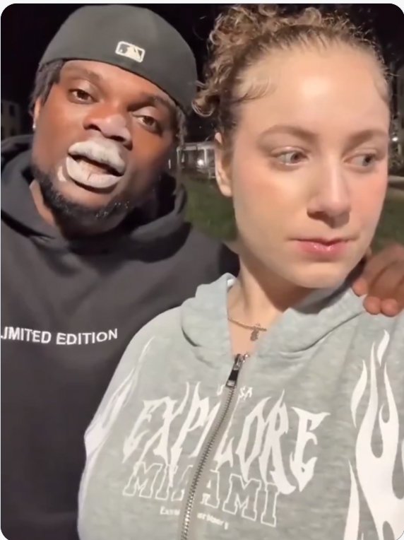 Man with smudged face cream pulls a silly face behind an unimpressed woman taking a nighttime selfie