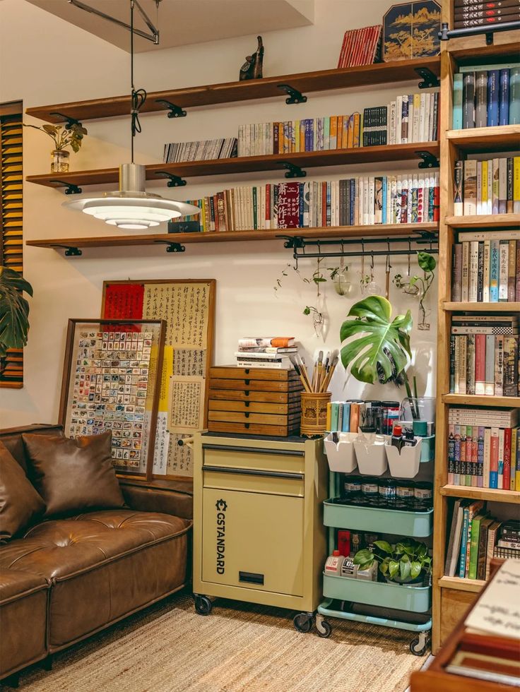 Cozy vintage home study nook lined with bookshelves, art supplies, leafy houseplants, and a tufted brown leather sofa