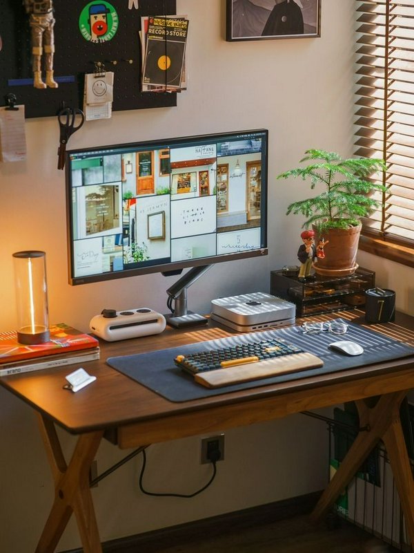 Warm curated home office wooden desk setup with monitor, mechanical keyboard, LED lamp, potted pl...