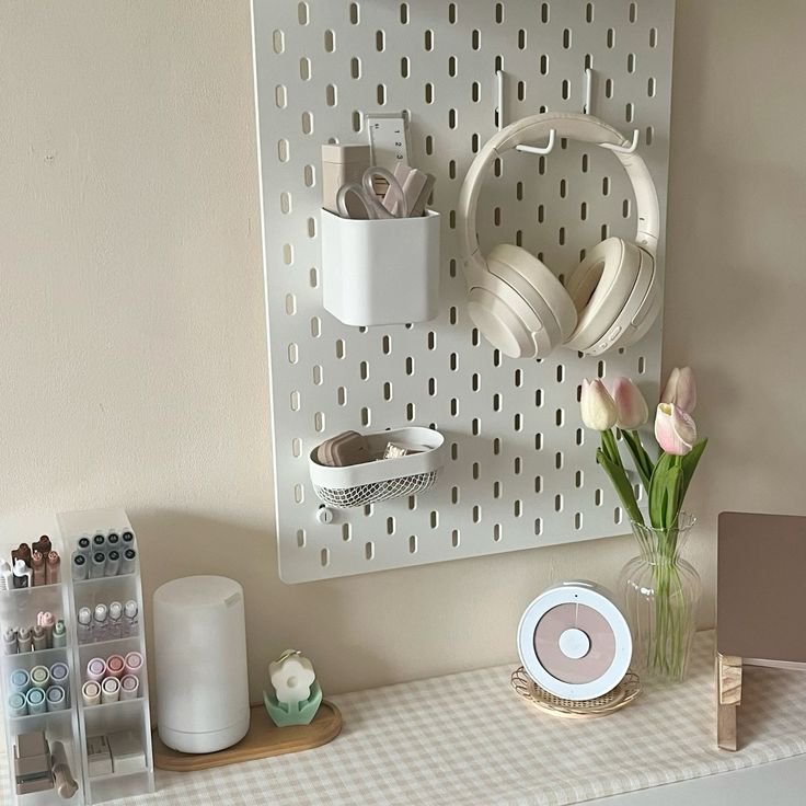 Cozy neutral desk setup with white wall pegboard, cream headphones, stationery storage, and soft ...