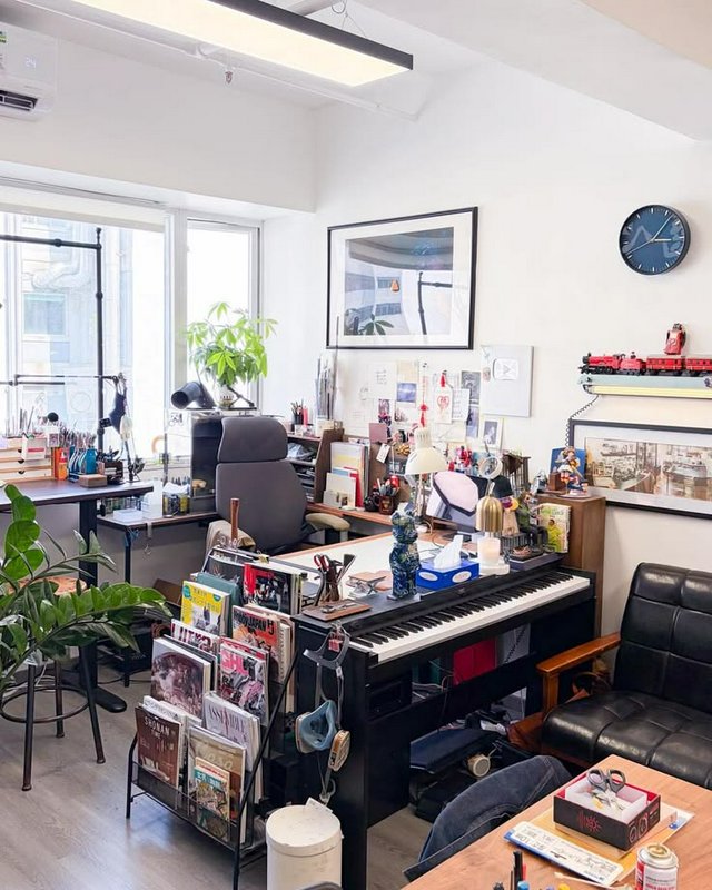 Sunlit eclectic creative home office workspace featuring a keyboard, art supplies, houseplants, b...