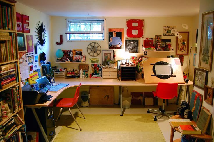 Eclectic cozy home art studio with curved work desk, red seating, wall decor, art supplies and bo...