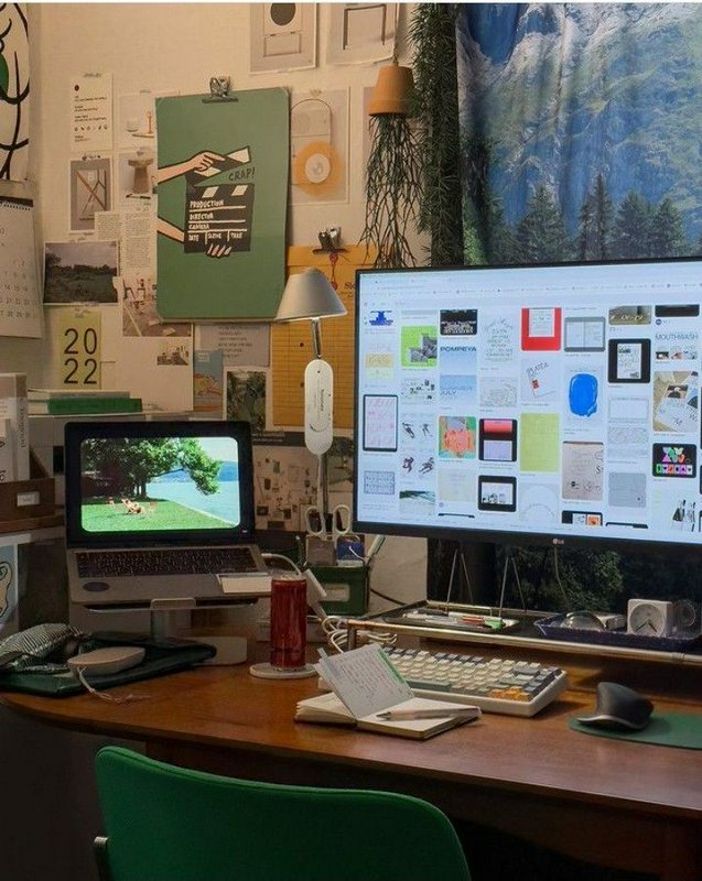 Cozy creative home office desk setup with dual displays, eclectic wall art, house plants, and a w...