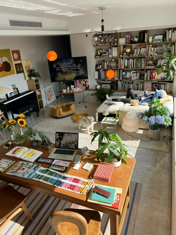 Sunlit cozy home art studio with craft supplies, a small dog, and a person relaxing on a plush sofa