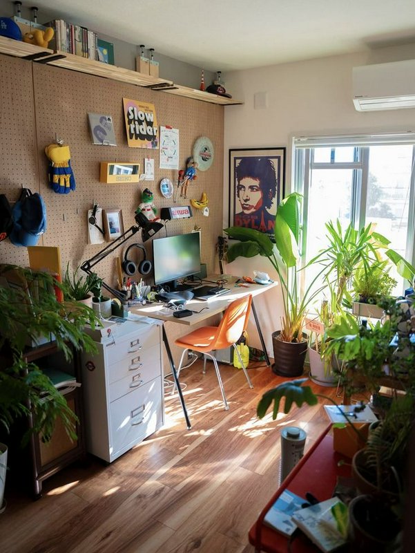Sunlit cozy plant-filled home office workspace with a desk, decorated pegboard wall, and warm nat...