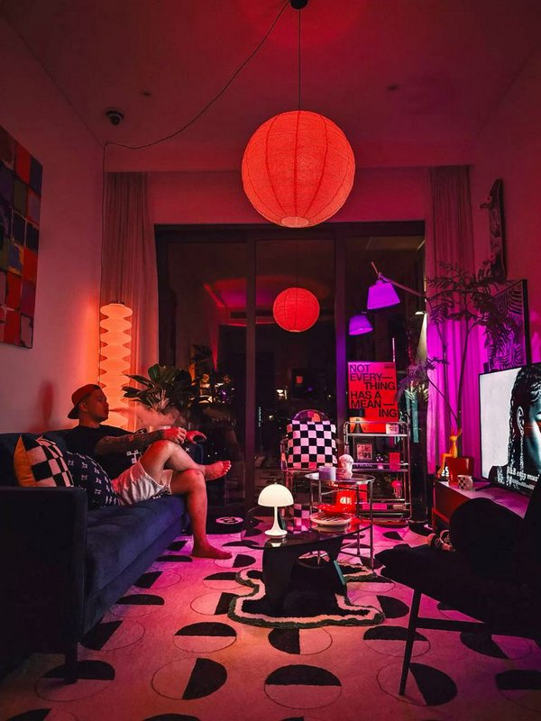 Man relaxing on a dark sofa in a vibrant pink neon lit maximalist living room at night