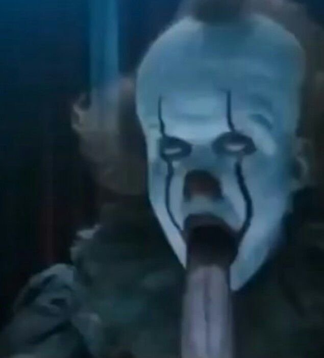 Blue clown mask with black tear lines and an elongated mouth in a dark, eerie scene.