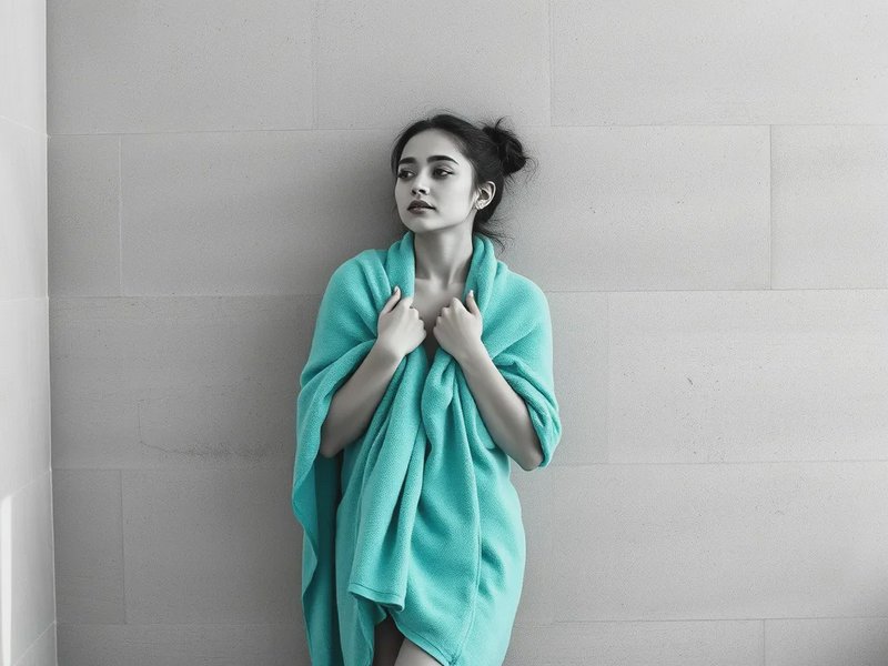 Woman wrapped in a turquoise towel against a pale tiled wall.