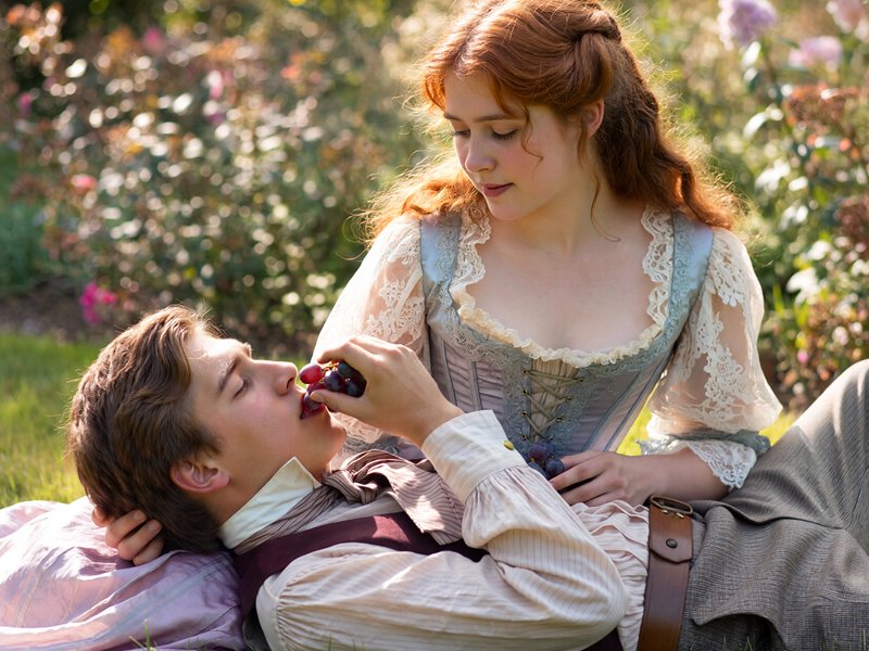 frozen in time by a hand-colored daguerreotype, the image shimmering with soft hues and silvery shadows, a young busty Victorian auburn woman and a dapper young man enjoy a picnic together, her ample bosom barely contained by her lacepunk Victorian corset dress, decolletage, teasing sensuality, he lays with his head cradled in her lap He wears a slight open ruffled shirt and trousers, he lays on his back whth his head on her lap, below her full breasts, she feeds him grapes, he lostens the ties on her blouse, exposing her nipples, they are in a floral garden setting with golden hour sunlight