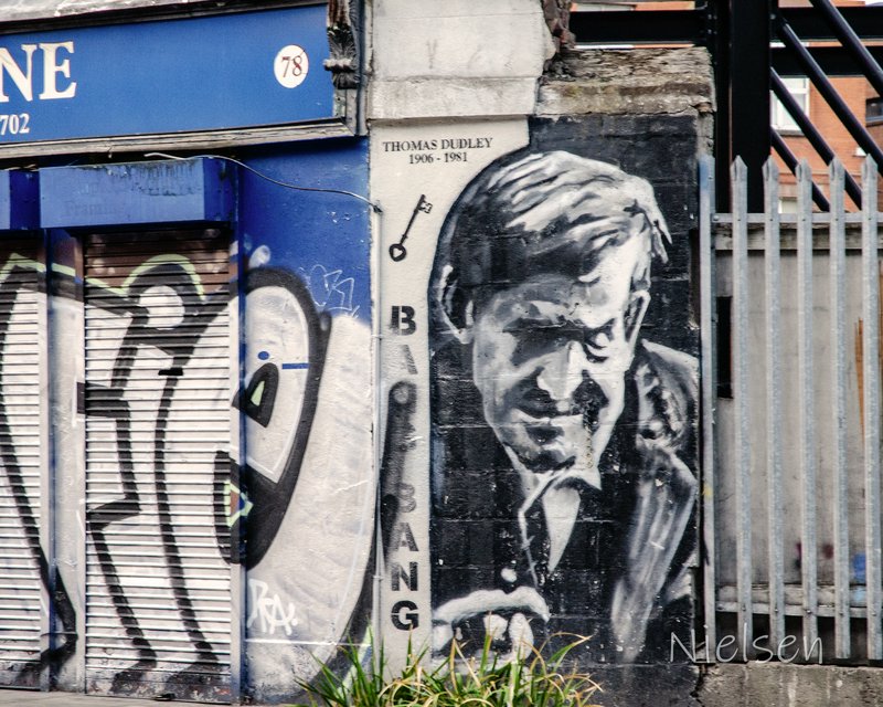 [Monochrome street art mural portrait of Thomas Dudley on a weathered urban building facade]