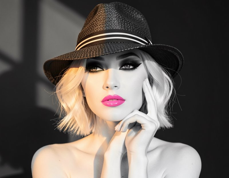 Closeup glamour portrait of woman in woven fedora hat with bold pink lipstick, dramatic selective studio lighting