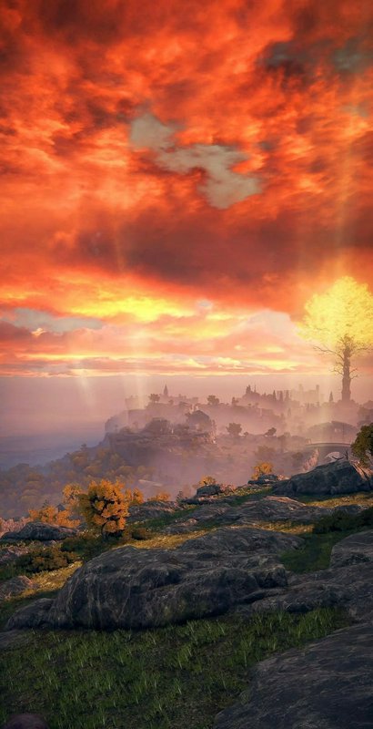 Fiery sunset over a rocky hillside with misty valley and distant ruins.