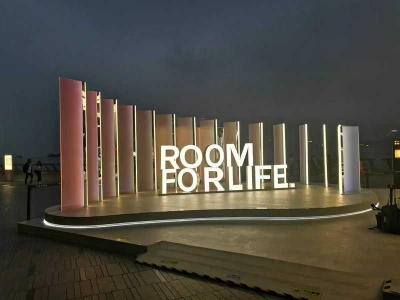 Nighttime outdoor stage with illuminated vertical panels and large letters spelling "ROOM FOR LIFE".