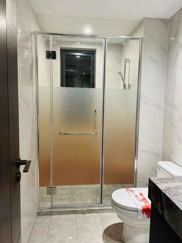 Modern glass shower enclosure with frosted gradient panels in a marble-tiled bathroom.