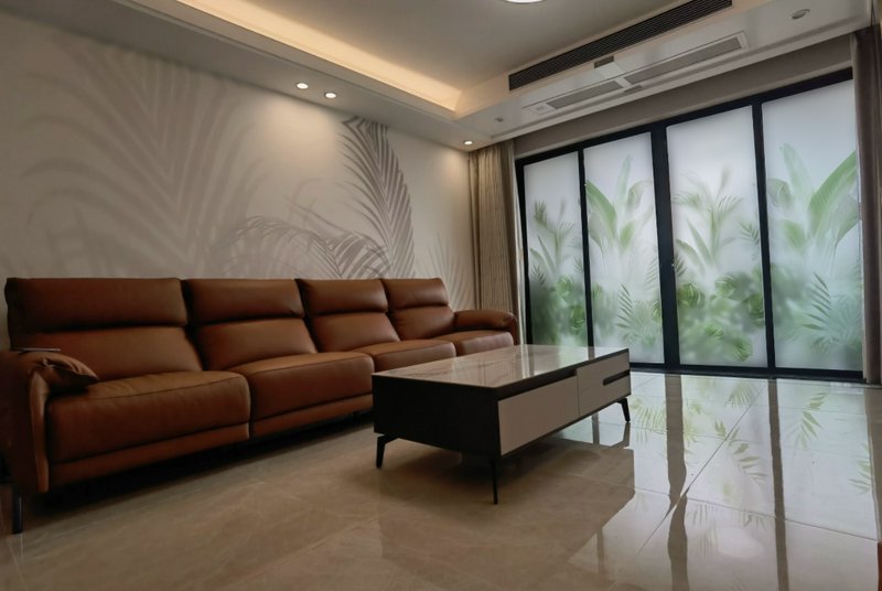 Modern living room with brown leather sectional, glass coffee table, and frosted palm-patterned w...