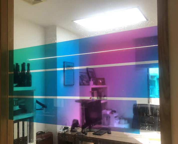 Office interior seen through a glass partition with teal, blue, and magenta color stripes.