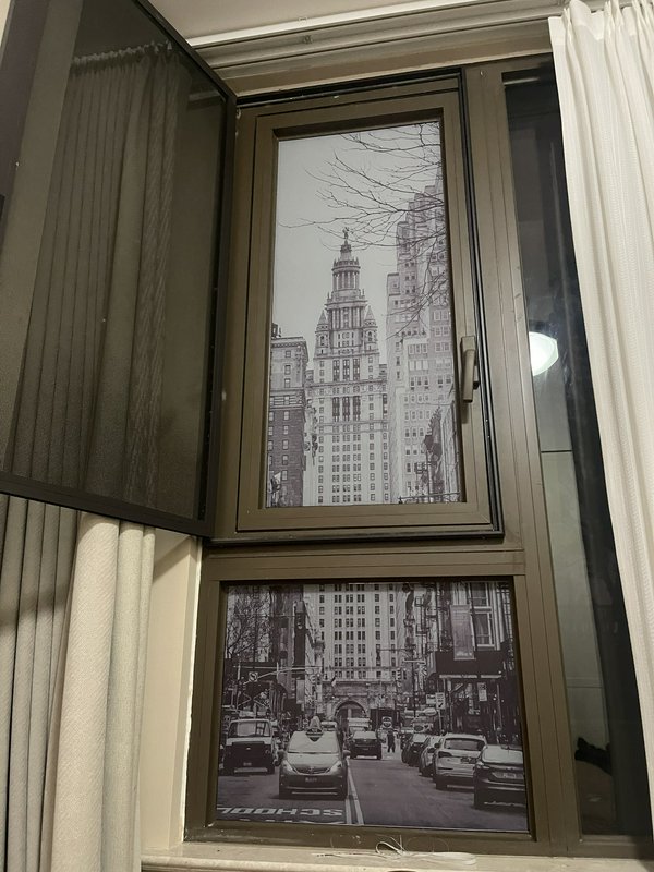 Window with two-pane grayscale cityscape artwork showing a tall skyscraper and a busy street.