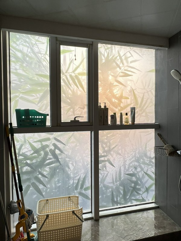 Bright bathroom shower area with frosted glass window featuring a bamboo leaf pattern and shelves...
