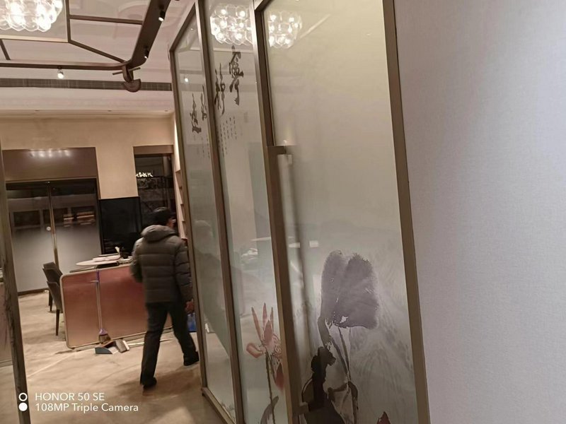 Interior of a modern restaurant with frosted glass panels featuring floral art and a person in a ...