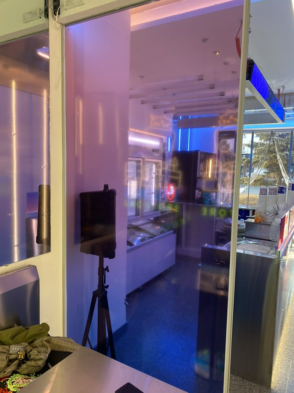 Neon-lit shop interior with glass doors, display case, and a tripod-mounted speaker.