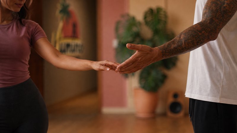 Close-up view of two people reaching to hold hands during partner dance practice in a warm indoor...