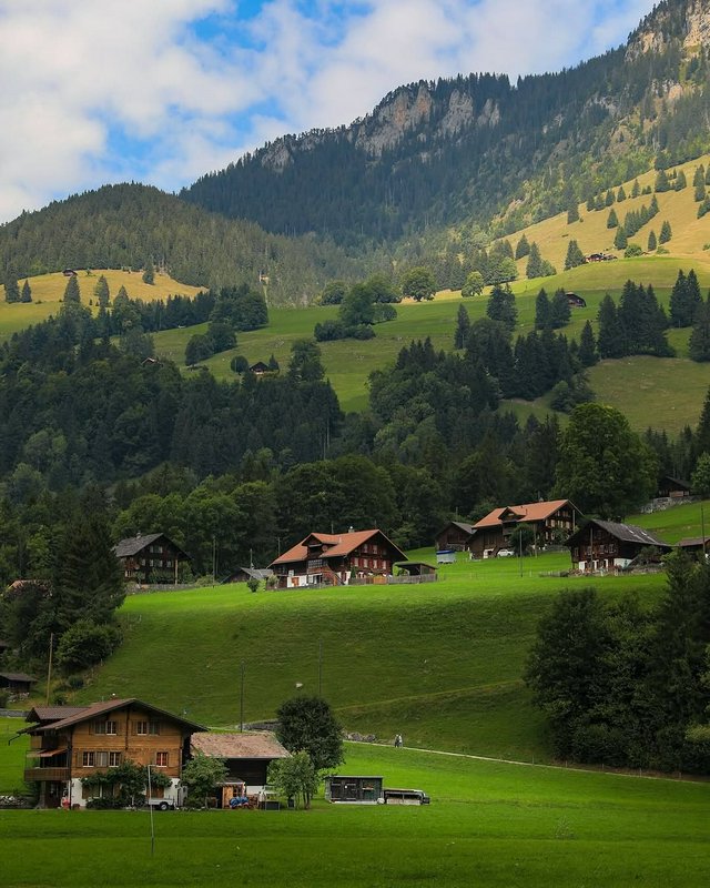 Scenic alpine village with wooden chalets nestled in green meadows and forested hills