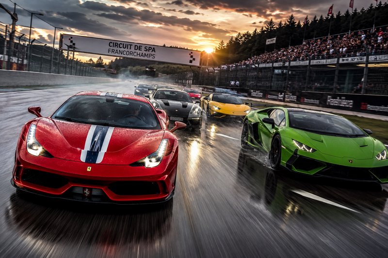 Supercars race side-by-side on wet Circuit de Spa Francorchamps track under a dramatic sunset sky.