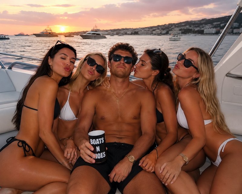Playful group of friends pose on a private yacht at golden sunset, women leaning around a shirtle...