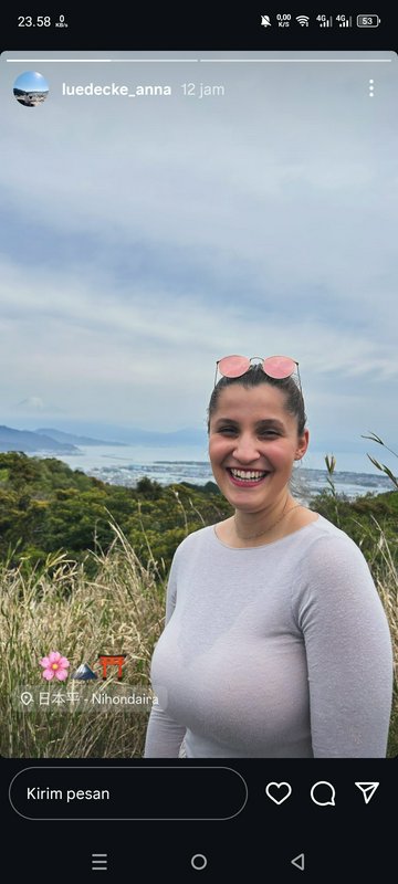 Smiling woman in a gray top outdoors with coastal hills and the sea in the background.