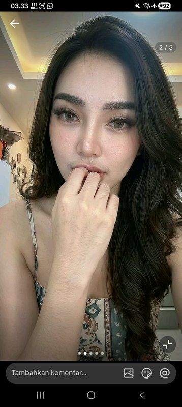 Close-up portrait of a woman with long dark hair and makeup, resting her hand near her lips.