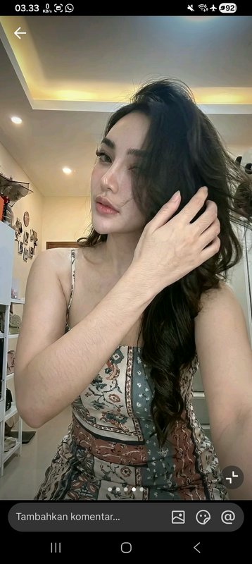 Portrait of a woman with long dark hair touching her hair indoors in a patterned sleeveless dress.