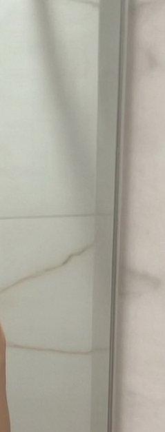 Close-up of a glass shower door with a metal frame and marble bathroom wall.