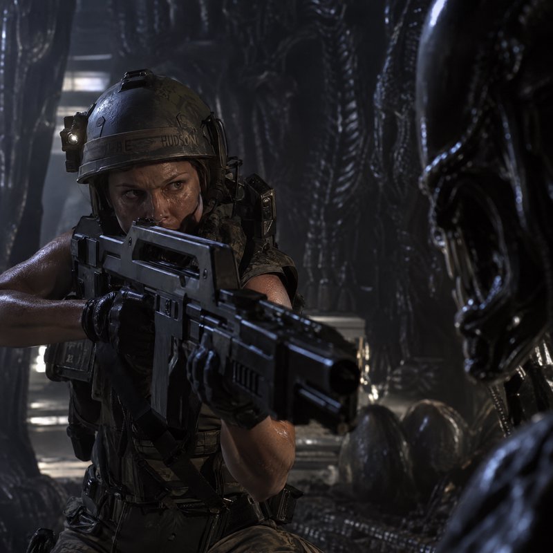 Female colonial marine aiming a pulse rifle at a menacing xenomorph inside an alien hive