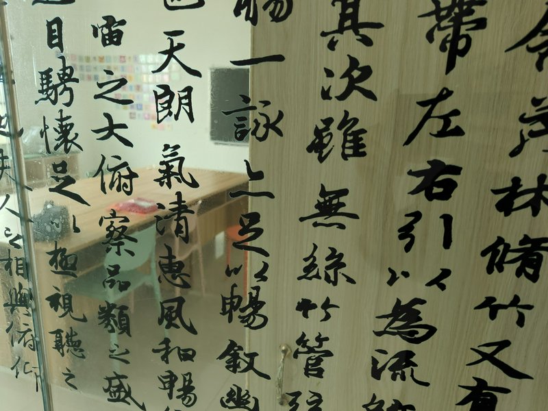 Glass wall with large black Chinese calligraphy characters in vertical columns, reflecting a brig...