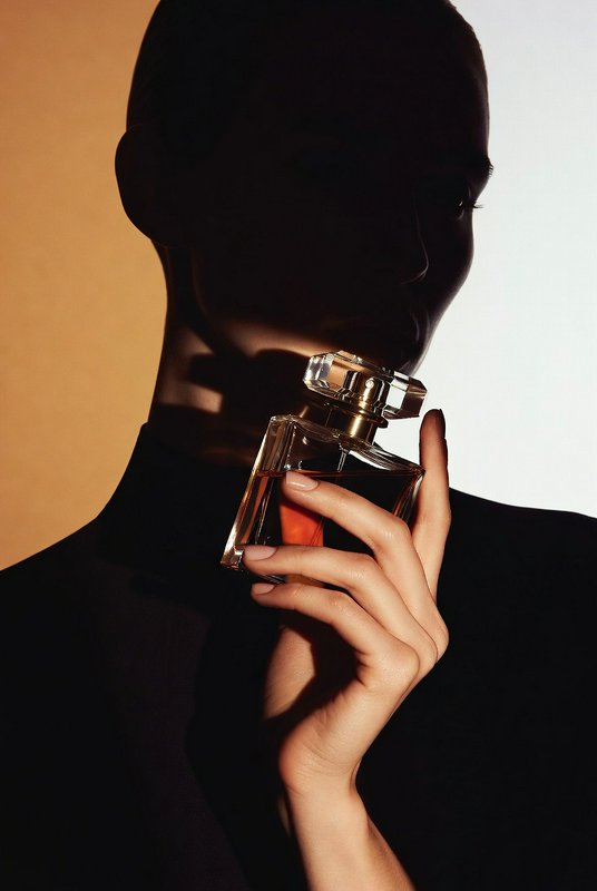 Silhouetted person holding a glass perfume bottle against a warm, split-toned background.