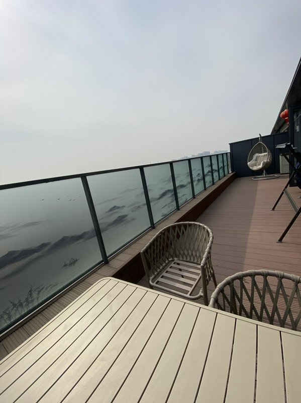 Rooftop balcony with glass railing, wicker chairs, and a table overlooking a foggy sea.