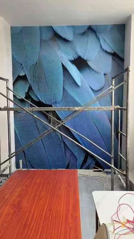 Construction scaffolding in front of a large blue feather-pattern mural on the back wall.
