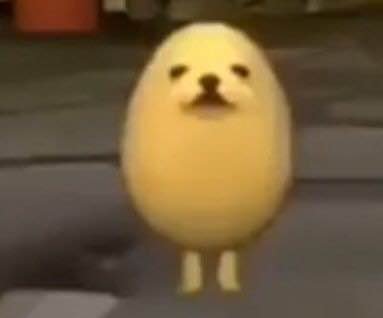 Cute yellow chick-like plush character with tiny legs on a street sidewalk.