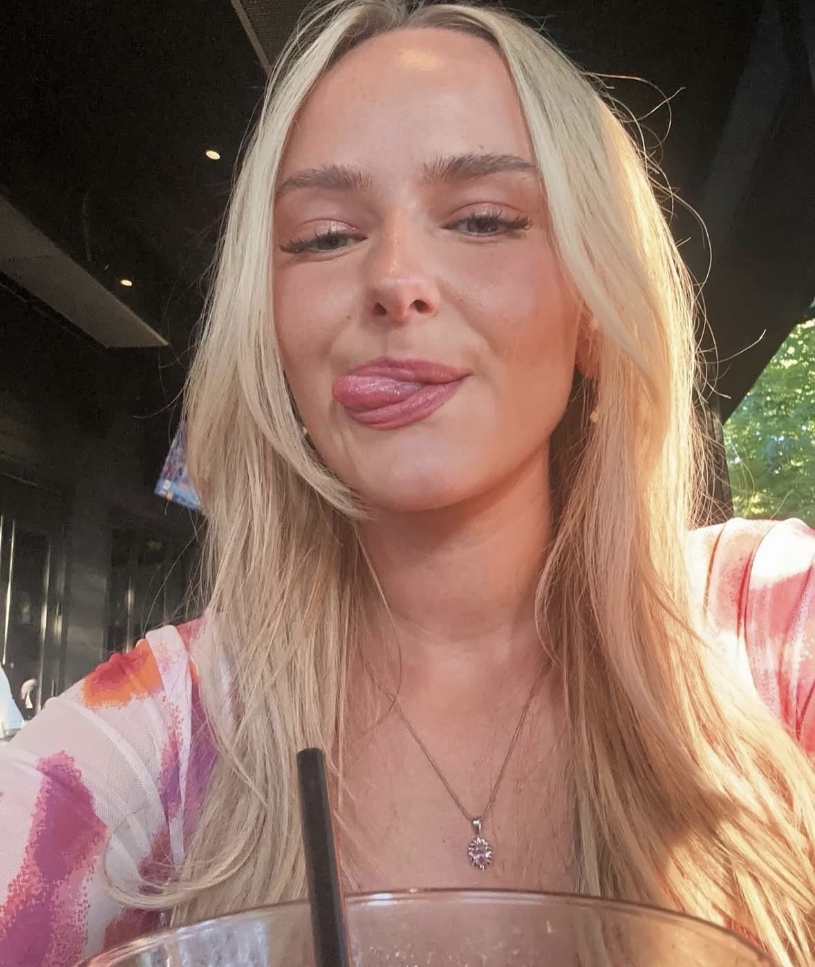 Young blonde woman sticking out her tongue in a playful outdoor selfie.