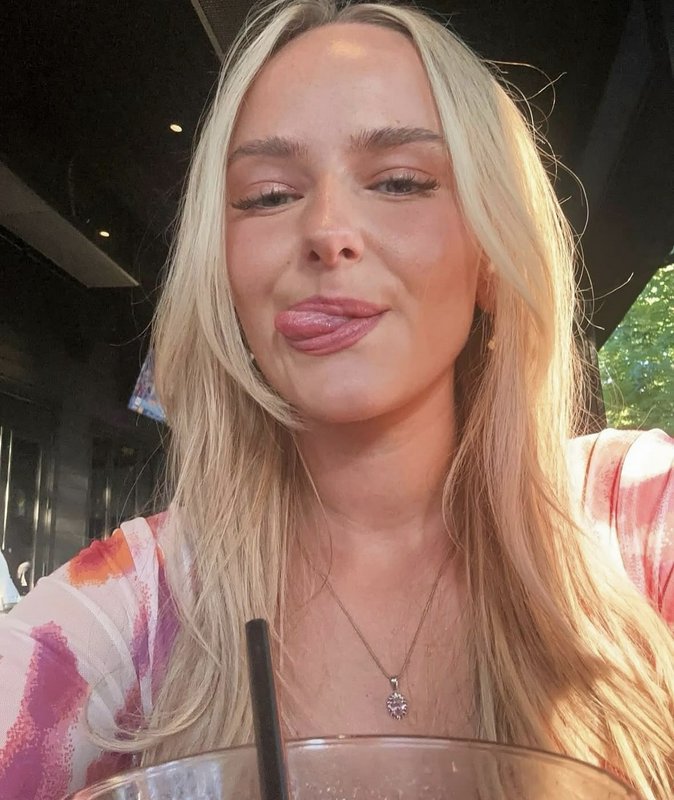 Young blonde woman sticking out her tongue in a playful outdoor selfie.