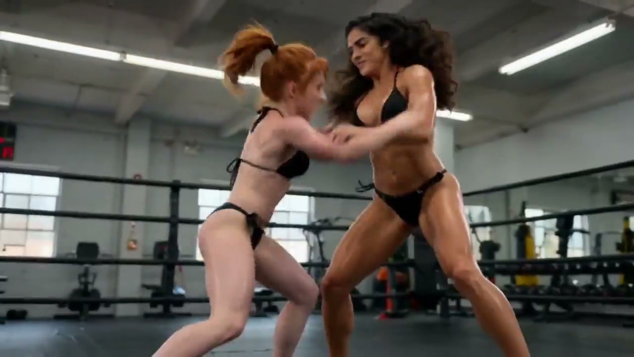 Two athletic women in black bikinis grapple while sparring in a gym boxing ring during wrestling ...