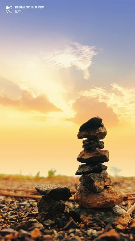 Stack of balanced stones on rocky ground at sunset with a warm, golden sky