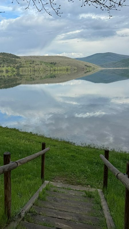 Scenic lakeside view with wooden steps leading to a calm reflective lake and distant hills.