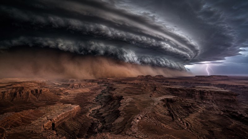 Massive rolling storm shelf cloud, dust haboob, and distant lightning loom over rugged desert canyon mesas