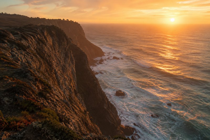 Sunset over rugged coastline cliffs with waves crashing below