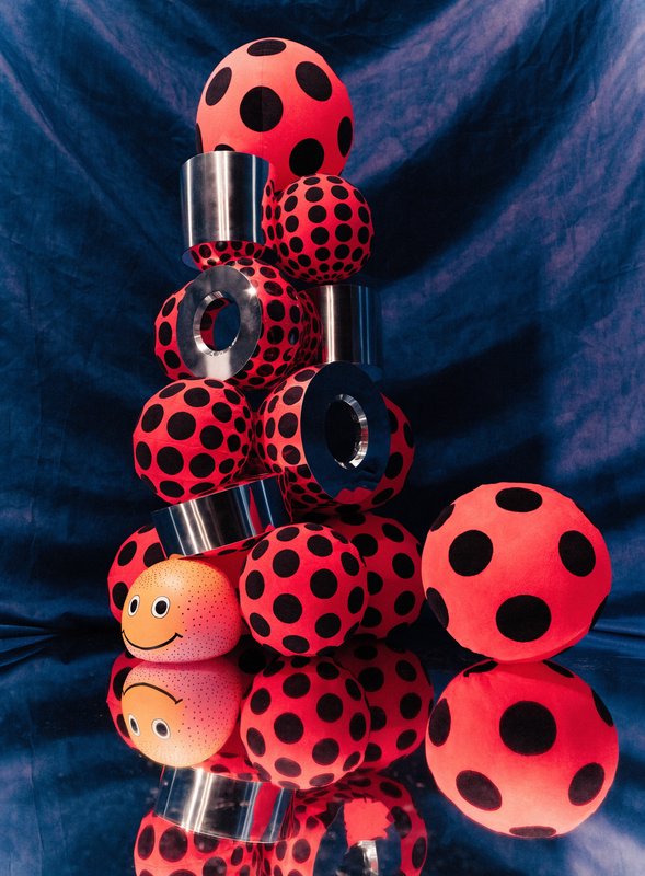 Stacked red black polka dot inflatable sculptures with smiley accent, mirrored on glossy surface ...